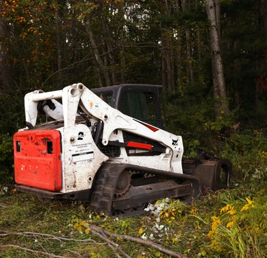 compact track loader opening an overgrown trail